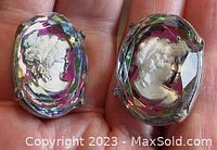 Close-up photo of the front of the earrings showing the oval faceted iridescent glass with white cameo profiles inside and purple base color.