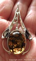 Front view of pendant held in hand showing amber cabochon and foliage design