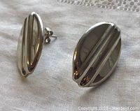 Front view of pair of oval sterling silver earrings with raised line design, shown on white fabric.