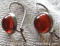 Front and side view showing round amber cabochon stones set in sterling silver with hook fastening, placed on woven fabric background.