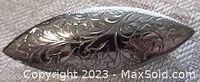 Close-up of front face of elongated marquise-shaped sterling silver brooch showing detailed floral engraving pattern and shiny polished finish.