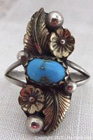 Close up photo of turquoise stone ring showing detailed flowers, feathers, and beads in sterling silver