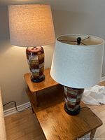 Two mosaic ceramic/glass lamps with cream fabric shades on wooden furniture