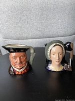 Two Royal Doulton Toby mugs representing Anne Boleyn and Henry VIII, side by side showing front and partial side views.