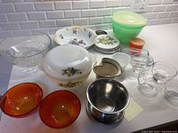 Overview of bowls and serving dishes showing the Arcopal white casserole with lid, clear and orange glass bowls, metal gravy dish, pottery dip dish, and Tupperware bowls with lids.