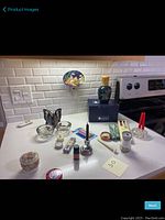 Overview of the varied candle and candle holder items on a kitchen countertop including Lampe Berger oil lamp, birthday candles, butterfly votive holders, and accessories.