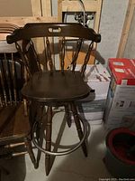 Photo of dark wood tall bar stool with curved backrest and circular footrest, showing wood grain and antique style.