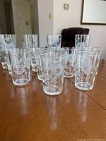 Front view showing multiple clear crystal glasses arranged with etched floral cornflower patterns including water, old fashioned, and juice glasses.