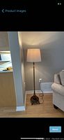Full view of floor lamp placed next to wall and sofa, showing lamp's wooden base and beige shade in context of room.