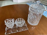 Photo showing the entire lot on a wooden table: cream pitcher, sugar bowl on tray, and large crystal canister with lid