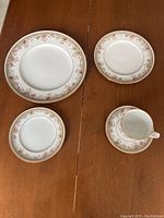 Set showing 4 types of pieces: dinner plate, luncheon plate, bread & butter/dessert plate, cup with saucer, all with matching floral and gold trim design.