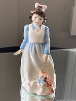 Front view of Royal Doulton Kitty figurine showing girl in white dress with cat at her side.