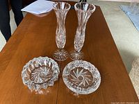 Four crystal pieces shown on a wood table: two tall bud vases and two low candy dishes, all with cut crystal patterns.