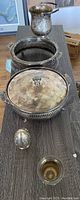 Full set of silver plated items on a dark table showing tarnished ice buckets, serving holders, and egg-shaped bucket.