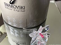 Figurine displayed next to its cylindrical Swarovski Silver Crystal box on reflective surface