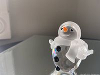 Close-up of Swarovski Silver Crystal Snowman figurine showing frosted head, scarf, mittens, orange nose and black crystal buttons with faceted body.