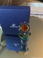 Front view of Swarovski sunflower crystal figurine with blue base and amber center, showing detailed petals and leaves.