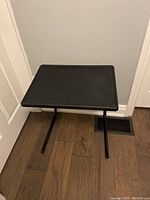 Black plastic top TV tray table with legs extended in one of three positions, showing the rectangular surface and metal tubular frame.