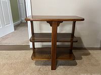 Full view of antique dark wood side table showing three shelves including the top, middle, and bottom surfaces, with a central vertical support.