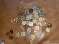 Top down photo showing a mixed collection of Euro coins of different denominations scattered on a brown surface.