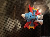 Photo of a vintage Smurf figurine in a hang gliding pose with red and yellow wings, blue skin and white pants and hat, made in Hong Kong.