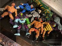 He-Man and assorted vintage Masters of the Universe action figures lying on a surface, showing a variety of colors and characters.