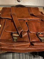 Front view of the brown leather briefcase featuring two buckle straps and multiple front pockets.