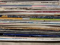 Stack of vinyl record spines showing various artist names and album titles with signs of wear and varied labels.