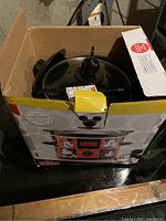 Photo of Mickey Mouse themed Crock Pot in original box showing black ceramic pot with glass lid and colorful Mickey Mouse graphics on box.