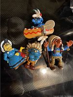 Photo shows four figurines: one Smurf in a canoe, one Native Smurf with spear and damaged nose, and two other Native American styled character figurines in blue and brown outfit.
