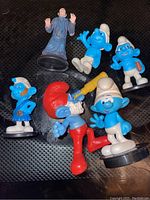 Photo showing six figurines from the Smurfs movie including four Smurfs characters and one human character in dark robe.