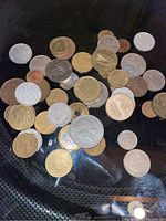 Photo showing a collection of 39 assorted old foreign coins spread on a dark surface. The coins have various designs and metals, including silver, gold, and bronze colors, representing multiple countries.
