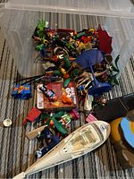 Photo showing large plastic bin filled with assorted Playmobil figures, a white helicopter toy, and various accessories scattered inside.