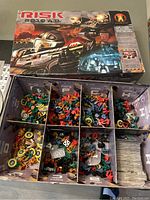 Top view of Risk 2210 A.D. box with cover art and compartments showing colored miniatures, tokens, dice, and cards inside.