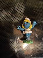 Photo of a Smurfette figure made in Hong Kong with characteristic blue skin, yellow hair, white dress and hat, and green base.