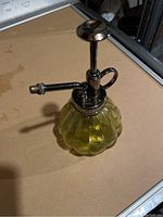 Yellow ribbed glass spray bottle with metal pump and spout nozzle placed on a flat surface.