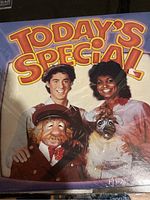 Front cover of the sealed vinyl record album from the children's show Today's Special, showing the title in large yellow and red letters and the image of four show characters including two human actors and two puppets.