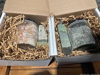 Two open cardboard boxes each containing one jar of bath salts and one bar of cold pressed soap surrounded by shredded paper packing.