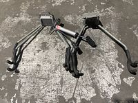 Two metal hanging bike racks and a manual tire pump placed on concrete floor showing hooks, mounting plates, and pump details.