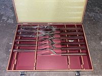 Full set of steak utensils laid in box with foam lid lining and wooden handle knives and forks in compartments