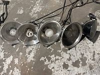 Set of five hanging utility lights with varied metal reflector shades lying on floor. Shows light cables and bulbs present in some lights.