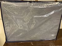 The bed inside a navy blue fabric bag with clear plastic panel on one side for viewing contents.