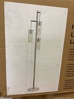 Image of the floor lamp and its design on the box; tall vertical lamp with three glass shades and polished chrome finish