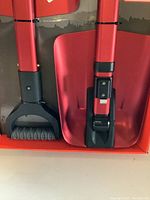 Close-up image of two red aluminum utility shovels with black handles and foldable blades in packaging.