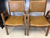 Front view of two wooden frame Mid-Century Modern chairs with mustard vinyl seat and back cushions, showing overall condition and style.