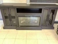Front view of dark gray wood media console with glass-front electric fireplace insert and side cabinets