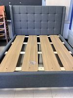 Front view of grey fabric upholstered queen bed frame with tufted headboard and five wooden slats.