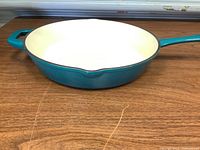 Side view of the large turquoise skillet showing the white interior surface and long handle
