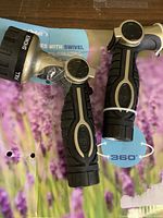 Photo of two new black and silver water hose nozzles with rubberized grip and swiveling connectors on a lavender floral background.