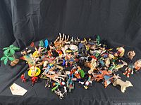 Wide-angle view of assorted vintage and used toy figures spread on a black fabric background including animals, humans, and fantasy characters.